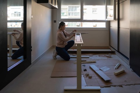A young Asian woman assembles a white desk in a modern home interior, illustrating a hands-on DIY