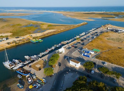 Harbour town with boats and a river flowing into the sea, lined with car parks and buildings,