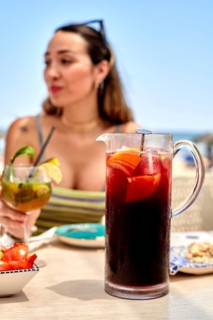 Group of friends relaxes at a beach side table on a sunny summer day. They enjoy colorful drinks,