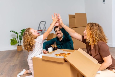Happy family celebrating moving day with high five, enjoying pizza and beer on the floor of their