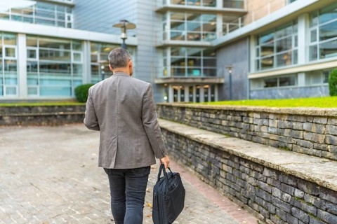 Rear view of a mature businessman with laptop bag walking in the city to work