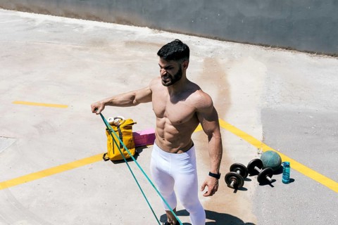 Fit man works out with resistance bands outdoors, showcasing muscular physique in a sunlit urban