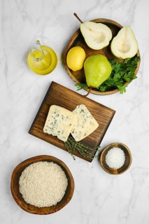 A marble countertop features fresh pear, herbs, blue mold cheese, rice, and olive oil, ideal for