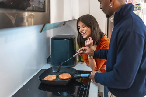 Young multiethnic couple preparing burgers on electric hob in modern kitchen, enjoying their time