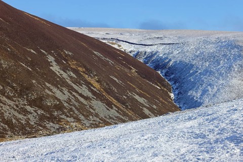 Gully and snow covered northside and sunlit southside of hills in the Strathdearn valley in winter,