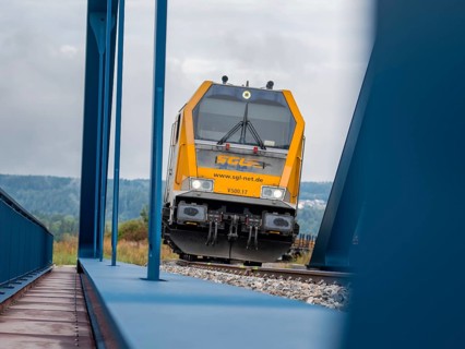 The driving trailer of a train on rails flanked by a blue bridge, track construction, rail delivery