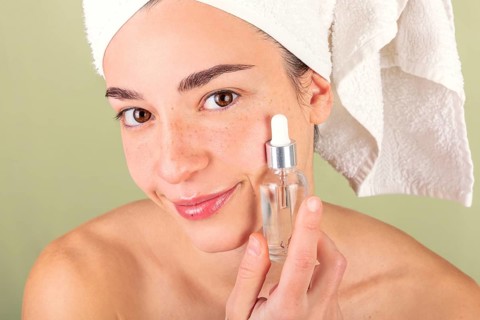 A woman applies a serum to her face, showcasing a skincare and self-care routine. Her hair is