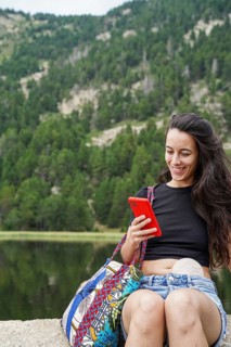 A woman with an ostomy bag is enjoying the outdoors, sitting by a lake, and smiling while looking