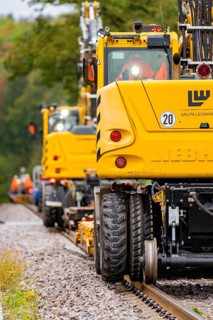 Yellow vehicles and workers on a railway line, surrounded by green foliage, track construction