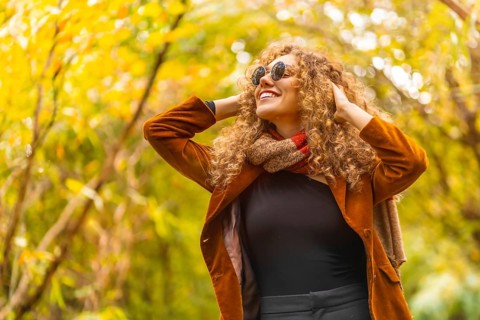 Woman wearing sunglasses and casual clothes looking up in a park during autumn