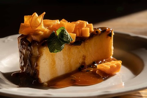 Glossy caramel cheesecake dessert topped with sliced fruit and a mint leaf, elegantly plated and