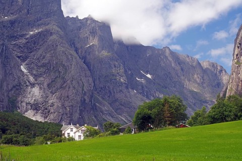 White house on a green field in front of impressive mountain formations and cloudy sky, Tom Cruise