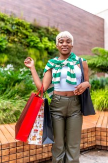 Vertical photo of a confident african woman carrying shopping bags outside a modern department