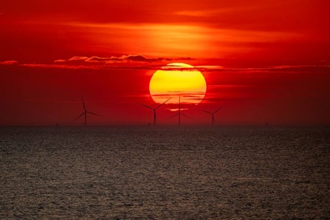 Dramatic sunset over the sea, wind turbines and wind turbines on the horizon, streaks of clouds,