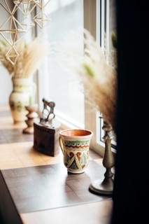 A warm and inviting windowsill adorned with an ornate mug, a pot, dried pampas grass, and vintage