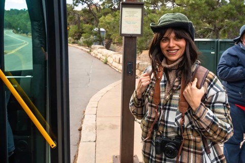 Young woman tourist with backpack and camera smiling while stepping off a public shuttle bus, ready