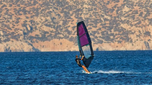 A windsurfer sails fast over the blue water in front of a mountain backdrop, windsurfer, Meltemi