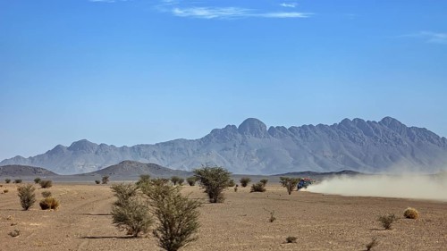 Off-road vehicle in a dusty desert landscape with mountains and trees, Off-road vehicle through the