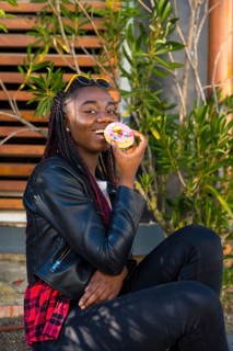 Vertical photo of a cool african teenager eating a doughnut sitting in the street alone