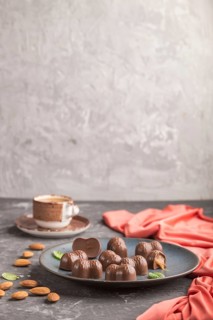 Chocolate caramel candies with almonds and a cup of coffee on a black concrete background and red