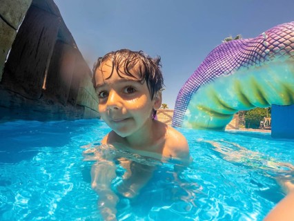 Young boy swimming in blue pool at water park, enjoying summer vacation on mediterranean sea in