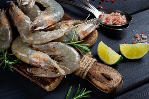 Fresh raw, white-footed shrimp, tiger prawns vannamei, on a wooden cutting board, with lime slices,