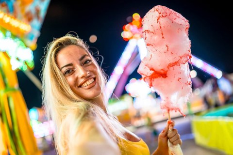 Blonde woman taking selfie holding pink cotton candy at night in an amusement park