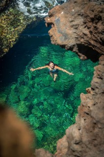 Young woman enjoying a refreshing swim in crystal clear blue green water, framed by rugged volcanic