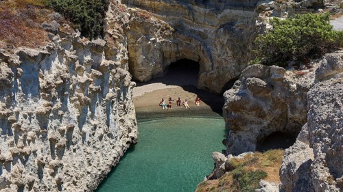 People swim through clear water between steep rock walls and a cave, volcanic island, island,