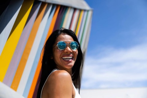 A cheerful woman in a vibrant outfit stands before a piece of modern architecture, creating a