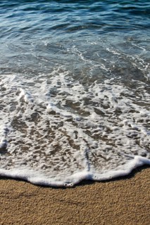 Close-up view of gentle waves washing over a sandy beach, capturing the serene movement of water