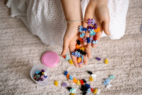 Hands holding colorful puzzle pieces over a carpet, suggesting playful creativity