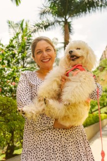 Happy mature woman holding and cuddling her fluffy white poodle dog while walking in a sunny park,