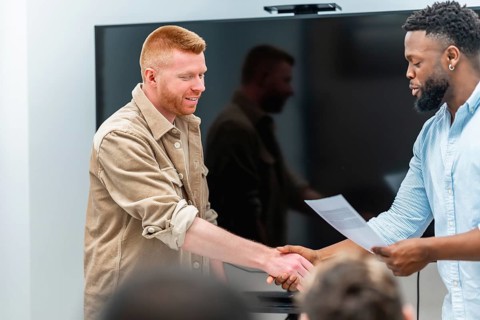 Two businessmen shaking hands after signing contract in a meeting room, celebrating successful deal