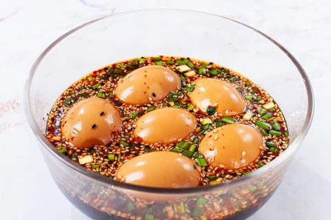 Five soft boiled eggs sit in a bowl filled with soy sauce, chopped green onions, and sesame seeds