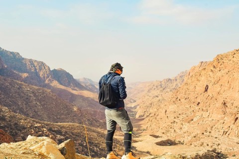 Man trekker standing on cliff edge using mobile phone network coverage vast sandstone valley
