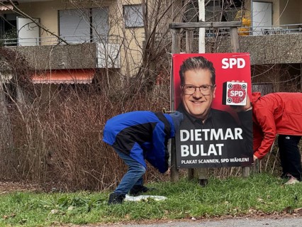 Two people, election workers, fix an SPD election poster on a green area in front of a residential