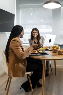 Two businesswomen enjoying breakfast and working on a laptop during their stay at a hotel