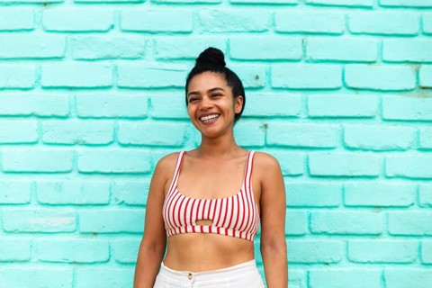 A joyful young Latina woman smiling brightly in a vibrant striped crop top, standing against a