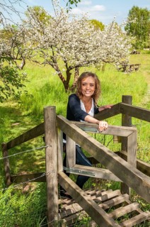 Young smiling woman opening a gate in a fence and with a blooming apple tree in the background in