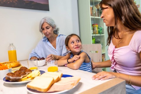 Multi generational women sitting around a kitchen table, enjoying a casual breakfast with food and