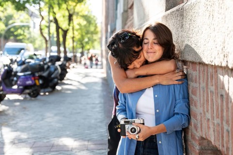 A multiethnic lesbian couple shares an affectionate embrace outdoors. The warm scene captures love