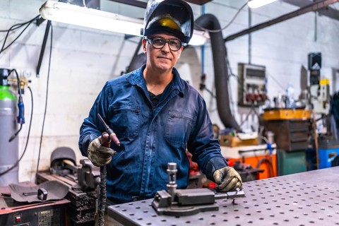 Mature welder standing in a metal factory taking a break and looking at camera