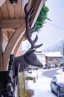 Wooden sculpture of a stag's head on a house in the snow, Enzklösterle, Calw district, Black