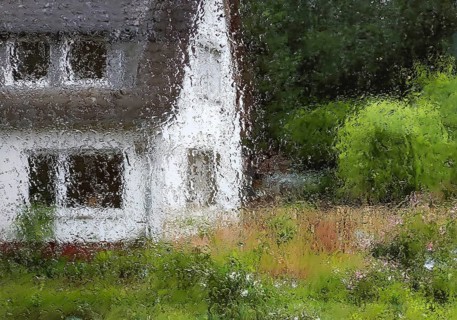 Raindrops on a window pane with indistinct view of a house with trees in summer, Witten, North