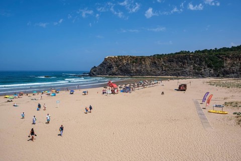 Extensive beach with cliffs in the background and people enjoying the summer weather, Odeceixe,