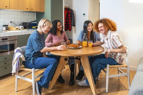 Four diverse roommates are sitting around a round kitchen table, laughing and enjoying breakfast