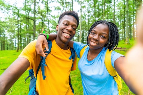 African cheerful young friends embracing taking a selfie in a green forest in springtime
