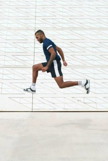Black athletic man captured mid-air in dynamic action against a modern geometric wall, showcasing
