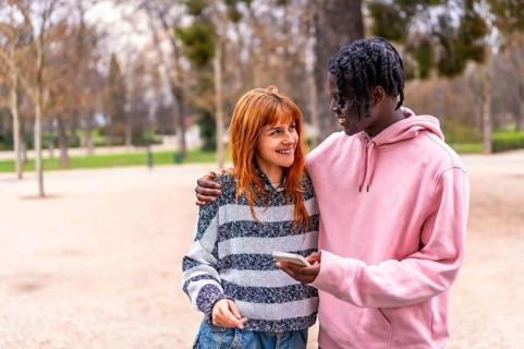 Happy multiethnic couple smiling and enjoying each other's company while using a smartphone in a